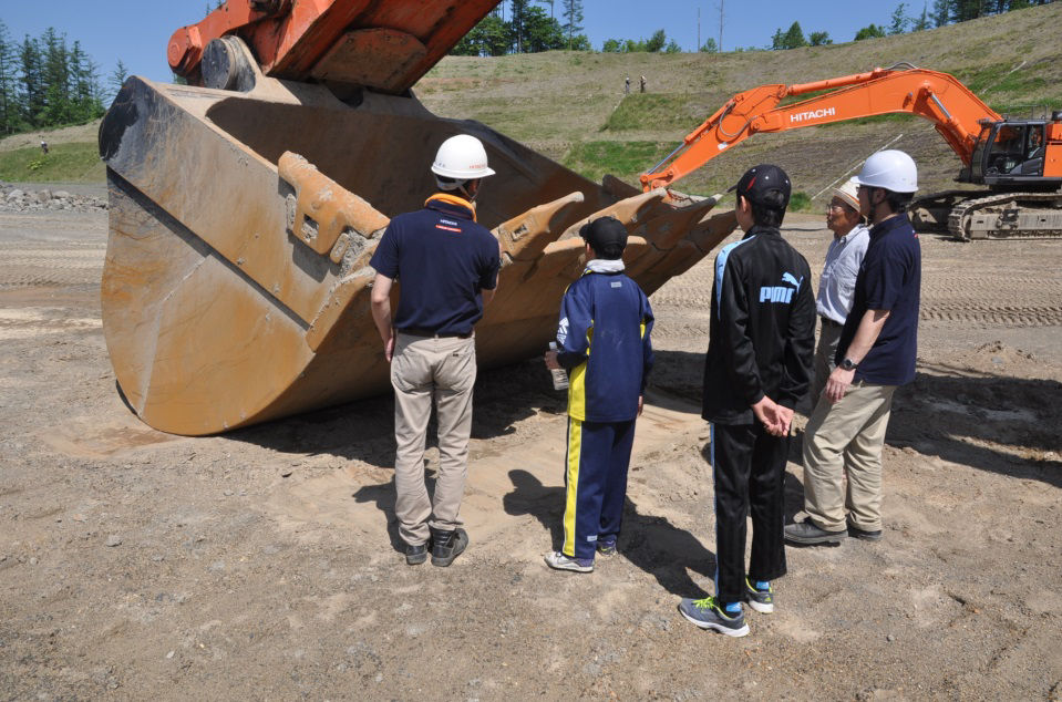 Students listen to an explanation about a large excavator and are amazed by the size of the bucket!