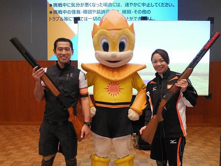 Company employee and para-cyclist Masaki Fujita (left) and trap shooter Yukie Nakayama (right), who both livened up the sports exhibit, strike a pose with Rey-kun (center)