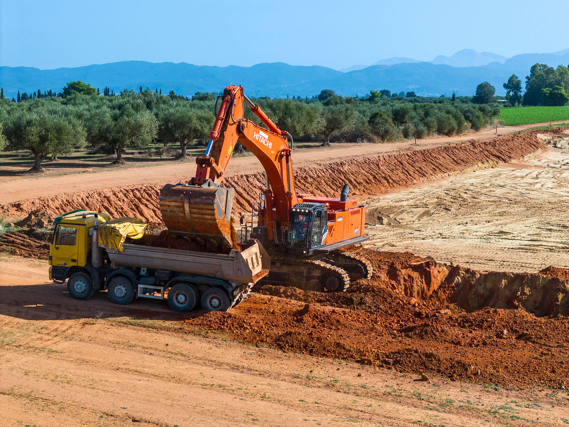 Side view of a Hitachi large excavator loading a truck on a road construction site in Greece